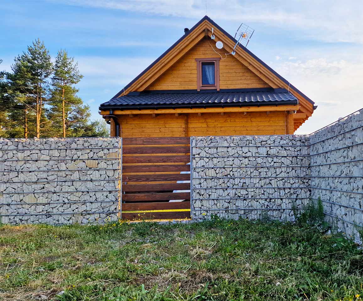 gabionový plot s drevom za ktorým stojí drevená chata